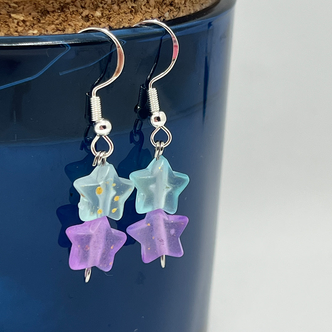 Star-shaped earrings with blue and purple stars on a blue background