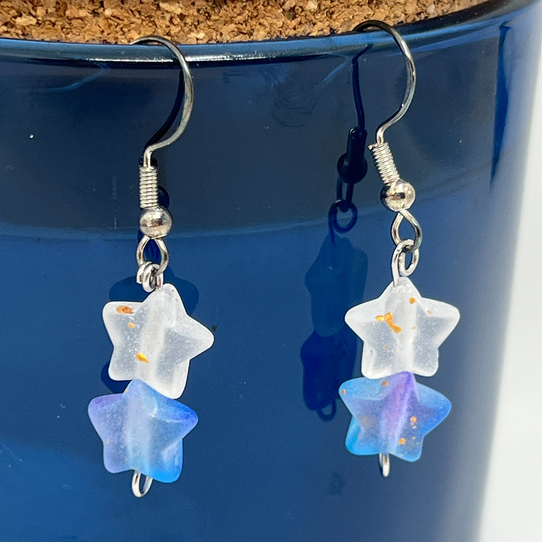 Star-shaped earrings with blue and clear stones hanging against a blue background.