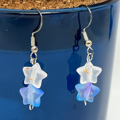 Star-shaped earrings with blue and clear stones hanging against a blue background.